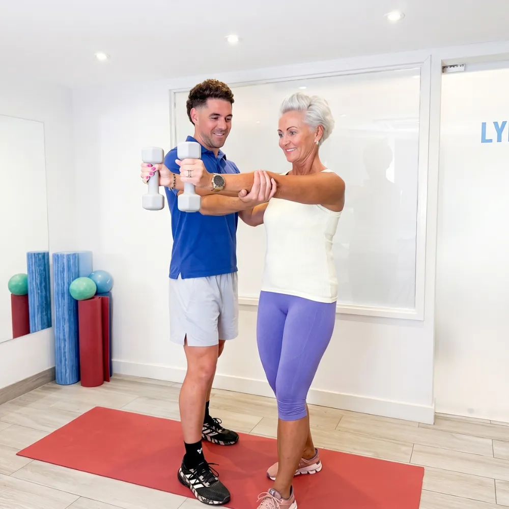 Nordic Balance physiotherapist guiding a woman through a standing dumbbell strength exercise.