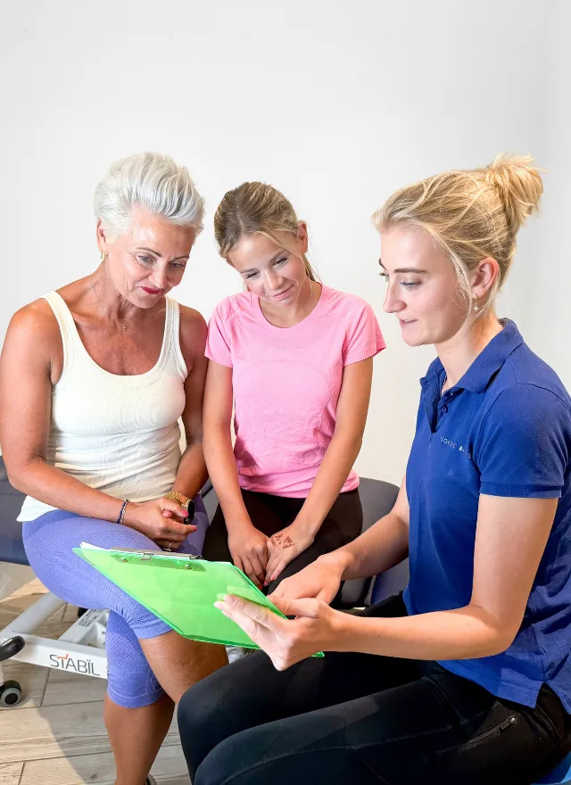 Nordic Balance practitioner explaining a treatment plan to two patients during a physiotherapy consultation.
