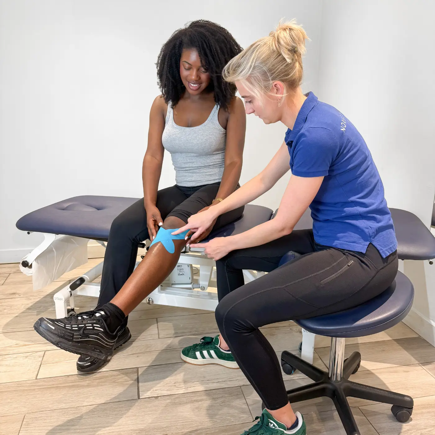Physiotherapist at Nordic Balance applying kinesiology tape to a woman’s knee during treatment.