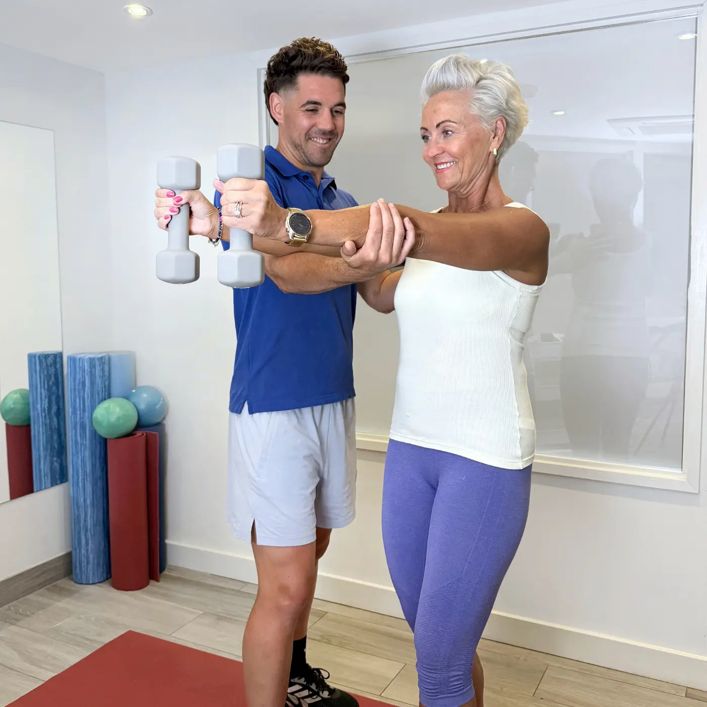 Exercise rehabilitation therapist at Nordic Balance guiding an older woman through an arm mobility exercise using a resistance band.