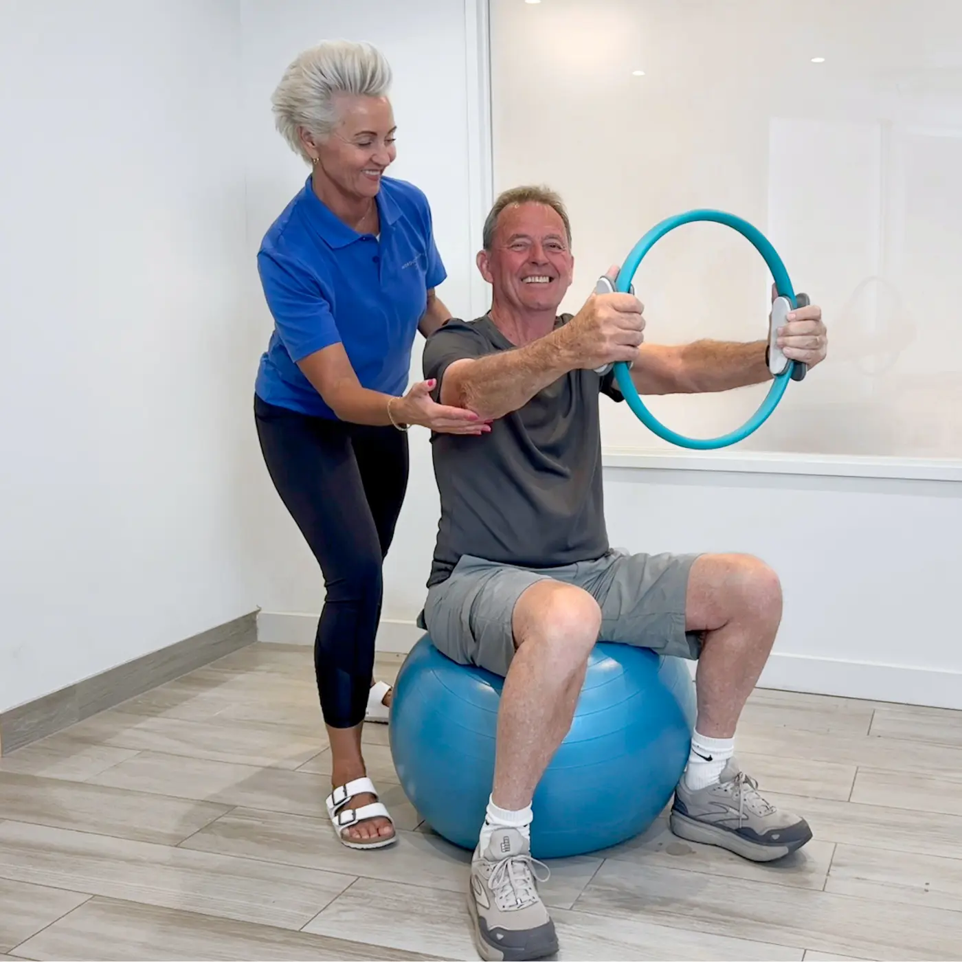 Physiotherapist helping an older man exercise with a resistance ring while seated on a stability ball at Nordic Balance.